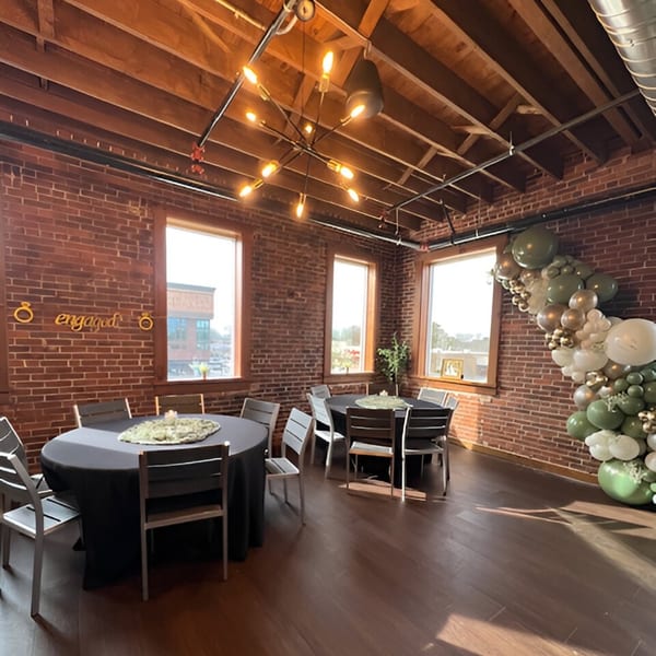 Hobo's event space with brick walls, exposed beams, round tables, and a balloon arch.