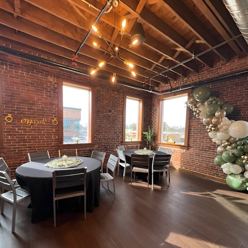 Hobo's event space with brick walls, exposed beams, round tables, and a balloon arch.