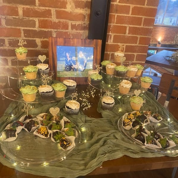 A dessert table with green and white cupcakes, chocolate-covered strawberries, and a framed photo.
