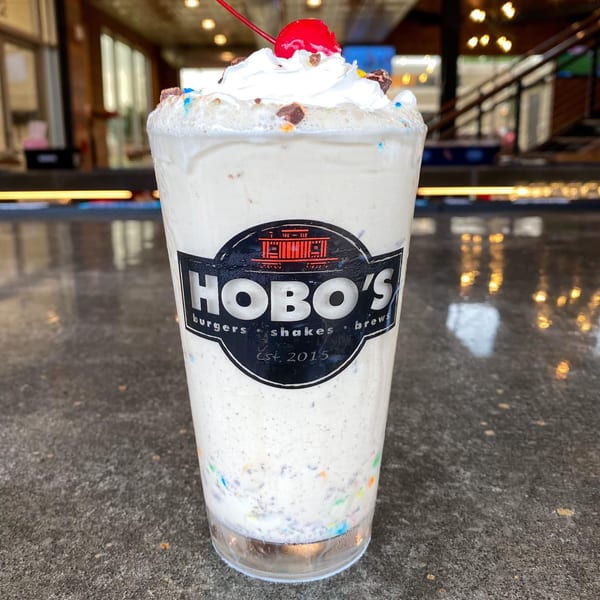 A Hobo's milkshake, topped with whipped cream, sprinkles, chocolate chunks, and a cherry.