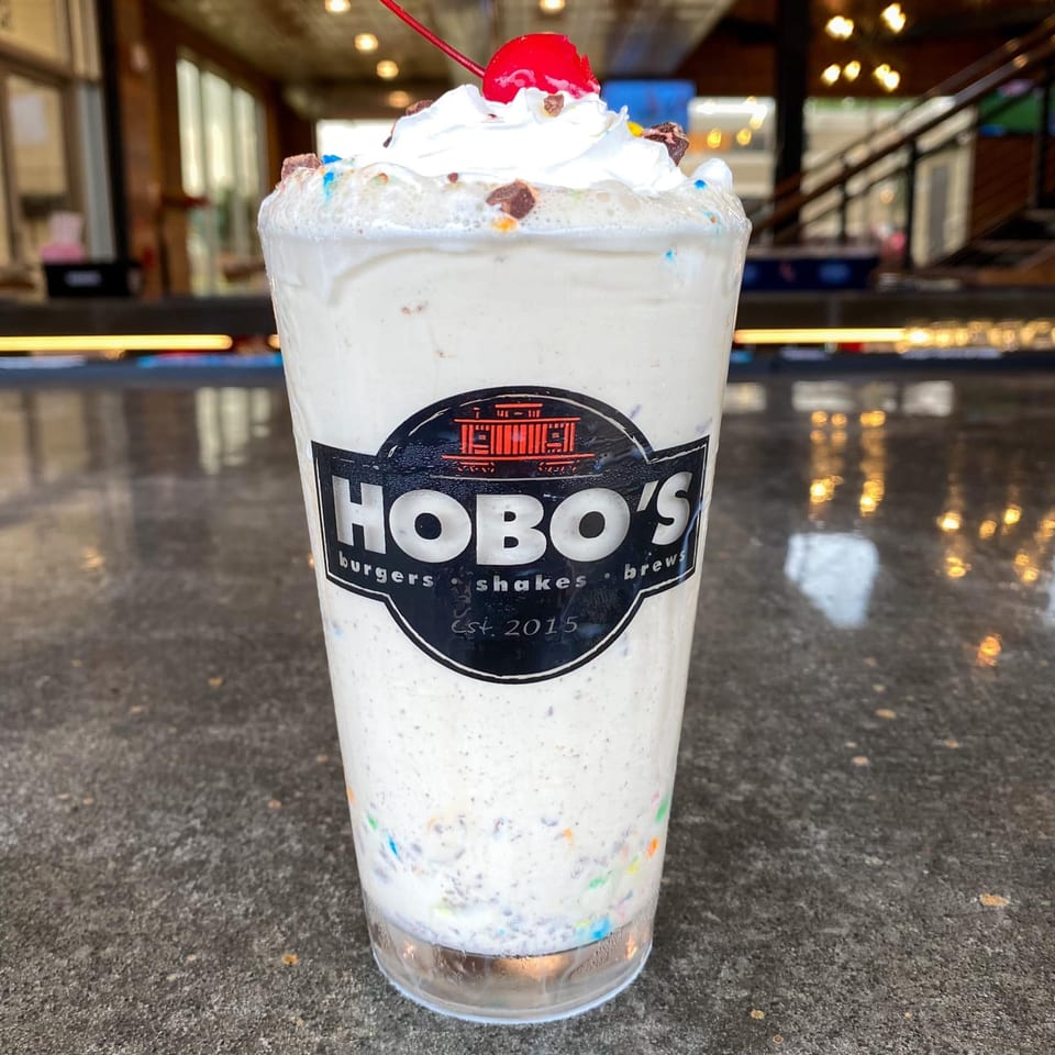 A Hobo's milkshake, topped with whipped cream, sprinkles, chocolate chunks, and a cherry.