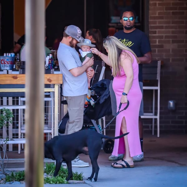 A family with a baby and a dog stands outside Hobo's, an American restaurant.