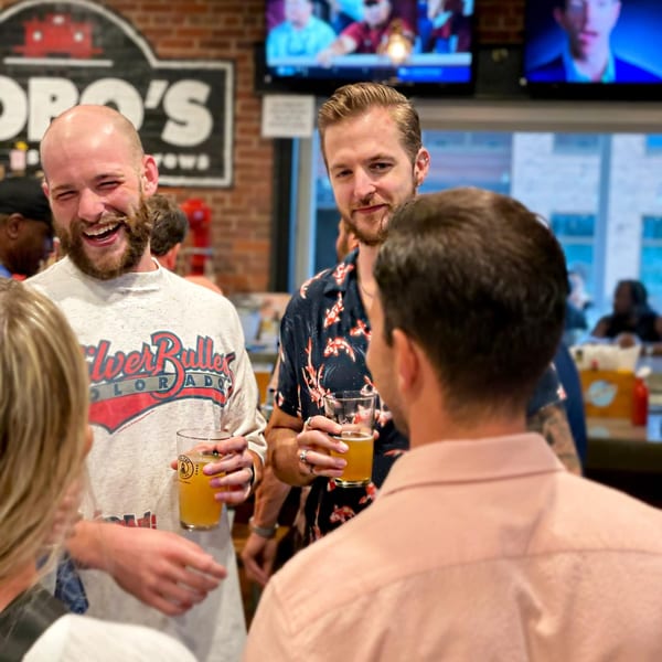 Three men, two holding beers, laughing and talking at Hobo's, an American restaurant.