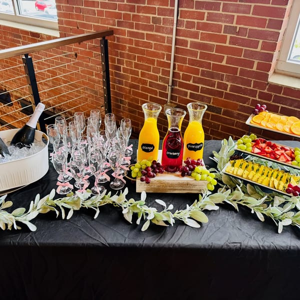 A mimosa bar with juices, champagne, fruit, and champagne flutes on a black tablecloth.