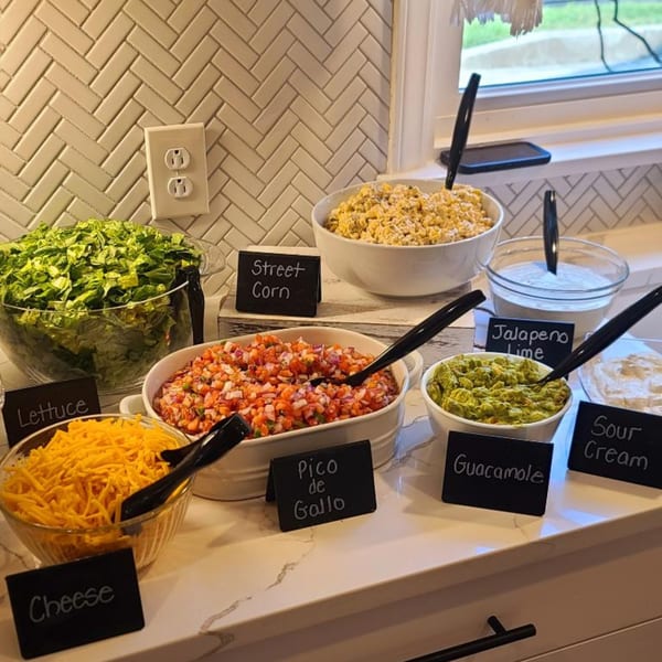 A Hobo's taco bar with bowls of lettuce, cheese, pico de gallo, street corn, guacamole, and sour cream.