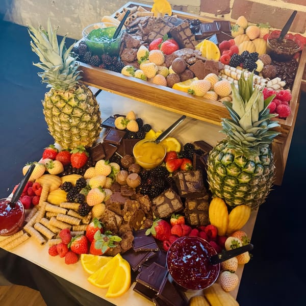 Two-tiered dessert board with pineapples, berries, chocolates, cookies, and various dipping sauces.