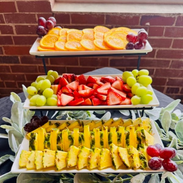 Three-tiered fruit display with sliced oranges, strawberries, green grapes, pineapple, and red grapes.