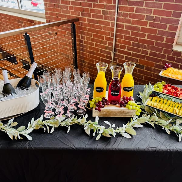 Mimosa bar with champagne, juices, fruit, and champagne flutes on a black tablecloth.