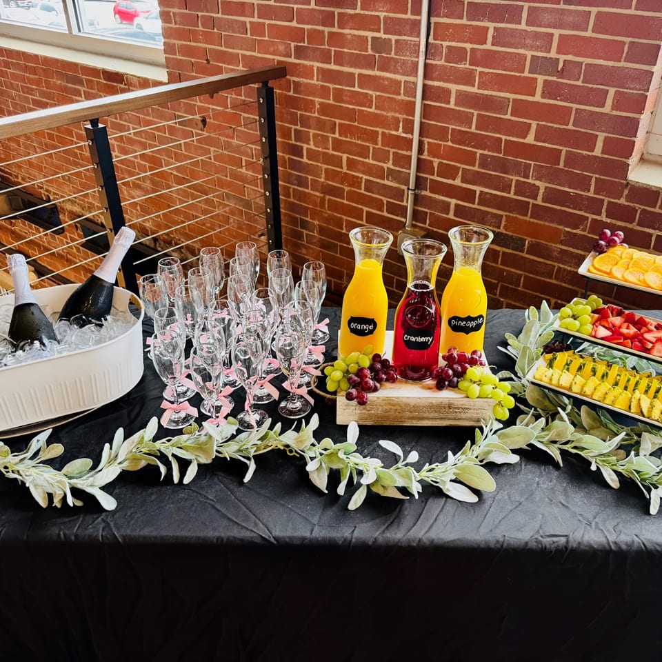 Mimosa bar with champagne, juices, fruit, and champagne flutes on a black tablecloth.