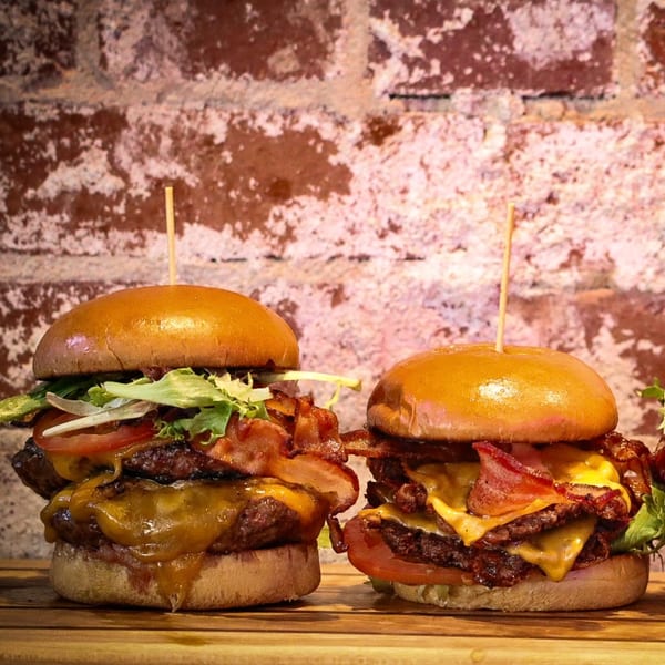 Two Hobo's double cheeseburgers with bacon, lettuce, and tomato on a wooden board.