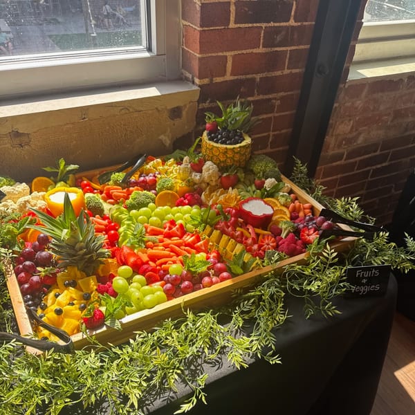A large wooden platter overflowing with colorful fresh fruits and vegetables, including pineapple, grapes, and carrots.