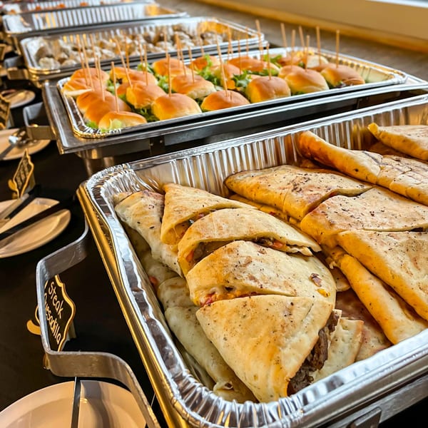 Hobo's catering spread with trays of mini sliders and steak quesadillas on a black tablecloth.