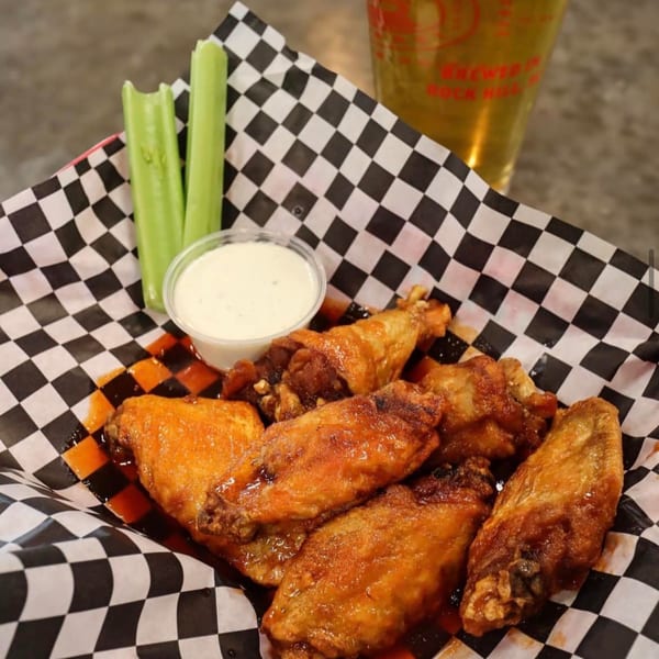 Hobo's American hot wings with celery sticks and ranch dressing in a checkered basket.